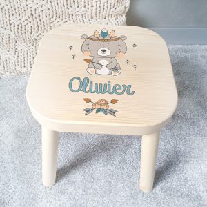 Taboret dziecięcy wykonany z jasnego drewna. Na siedzisku ma uroczą grafikę, która pochodzi z kolekcji Miś Indianin.