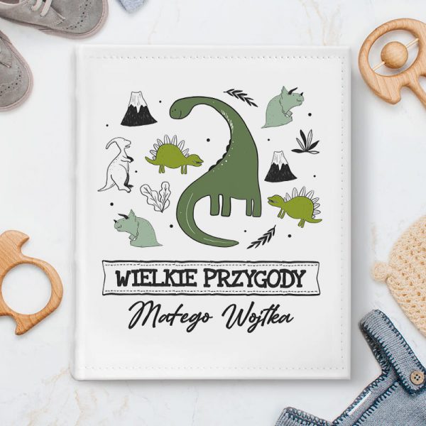 Album pamiątkowy na pierwsze wspomnienia dziecka. Białe tło z imitacji skóry ozdobiliśmy prehistoryczną grafiką zielonych dinozaurów. Poniżej napis Wielkie przygody małego i odmienione imię dziecka.