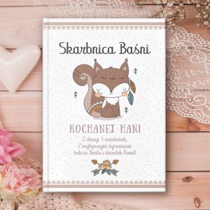 Biała książeczka z grafiką na okładce. Przedstawia ona wiewiórkę z indiańskimi piórkami oraz dedykację od bliskich. Tło w drobne pastelowe kropeczki.