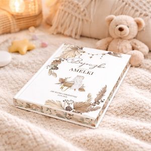 Książka "Bajeczki napisane dla Amelki" leży na miękkim kocu obok pluszowego misia, otoczona dekoracjami w pastelowych kolorach, w tym gwiazdkami i słodyczami.