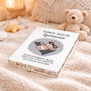 Książka dla dzieci z tytułem "Pierwsze bajeczki Tymona", na okładce wizerunek wiewiórki w przebranie. W tle pluszowy miś i jasne poduszki.