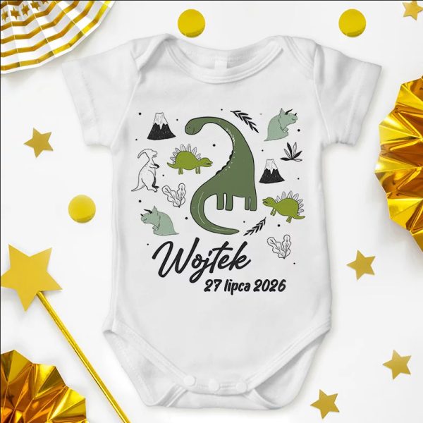 Biały body niemowlęce z ilustracjami dinozaurów, gór i roślin, z imieniem 'Wojtek' oraz datą '27 lipca 2026' na przodzie, otoczone złotymi gwiazdkami i dekoracjami w tle.