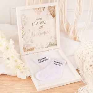 Białe skarpetki z napisem "Będziesz Dziadkiem" w eleganckim pudełku z kwiatowym motywem i napisem.