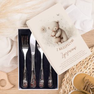 Zestaw sztućców w eleganckim opakowaniu, zawierający trzy widelce i nóż, z rysunkami misiów na uchwytach, położony na jasnym tle z elementami tkanin i małych butów dziecięcych.