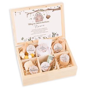 niezbednik-boho-dla-dziewczynki-z-imieniem Drewniane pudełko z różnymi dekoracyjnymi przedmiotami, w tym monetą, małymi kostkami i wstążkami, z wewnętrzną kartką z życzeniami dla noworodka. Wnętrze podzielone na sekcje, każda z innym przedmiotem oznaczonym napisami takimi jak 'Na Pamiątkę' i 'Na Szczęście'.