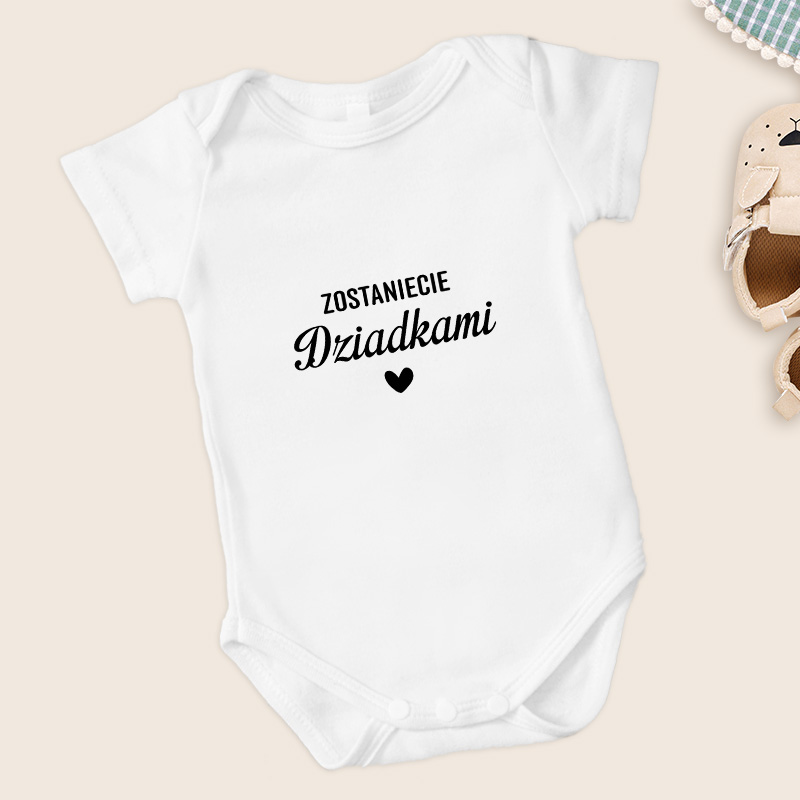 Biały body niemowlęce z napisem "Zostaniecie Dziadkami" w czarnym kolorze oraz małym serduszkiem.