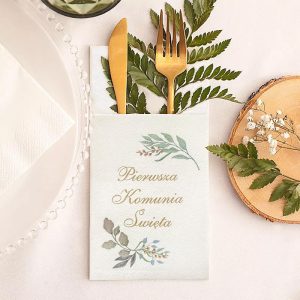 Elegancka serwetka na stół z napisem "Pierwsza Komunia Święta" oraz złotymi sztućcami i liśćmi dekoracyjnymi.