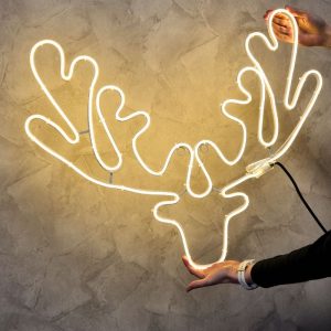 Neonowa lampa w kształcie poroża, trzymana przez osobę, na tle teksturowanej, jasnej ściany.