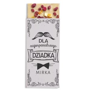 Opakowanie czekolady z napisem 'DLA najwspanialszego DZIADKA' i dodatkami, takimi jak maliny i popcorn, na białym tle z ozdobnym czarnym wzorem.