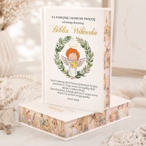 Biblia z ilustracją aniołka w wieńcu, z tekstem upamiętniającym chrzest i komunię, na jasnym tle.