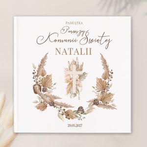 Biała okładka pamiątki Pierwszej Komunii Świętej z napisem 'Pamiątka Pierwszej Komunii Świętej Natalii' i datą '29.05.2027', ozdobiona delikatnymi, pastelowymi roślinami i krzyżem w centralnej części.