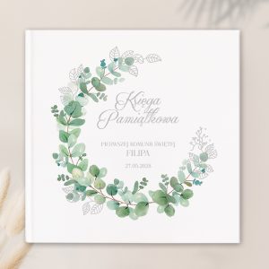 Okładka księgi pamiątkowej z delikatnymi, zielonymi liśćmi ułożonymi w kształt koła, z napisem 'Księga Pamiątkowa' oraz informacją o Pierwszej Komunii Świętej Filipa z datą 27.05.2028.