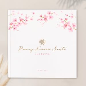 Okładka książki z napisem "Pierwsza Komunia Święta" oraz imieniem "Juleczki" w złotym kolorze. W górnej części ozdobionej różowymi kwiatkami. Data "10 MAJ 2027" na dole.