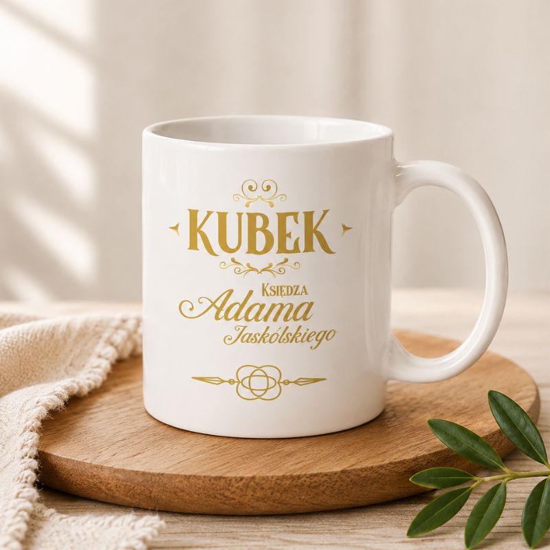 Biały kubek z złotym napisem "KUBEK Księdza Adama Jaskólskiego" na jasnym tle, znajdujący się na drewnianym talerzu.