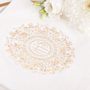 Komunijne serwetki ozdobne w kolorze białym. Na środku grafika złotej hostii zdobionej ażurowym wzorem dookoła. Elegancka dekoracja stołu komunijnego.