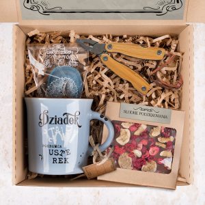 Zestaw prezentowy w kartonowym pudełku, zawierający niebieską filiżankę z napisem 'Dziadek', drewniane nożyce ogrodnicze, paczkę z kruchymi ciasteczkami oraz pudełko z suszonymi owocami i napisem 'Słodkie podziękowania', wszystko ułożone na wypełnieniu z papierowej smyczy.