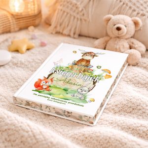 Książka zatytułowana "Księga bajek Adasia" leży na jasnym, miękkim tle z elementami dekoracyjnymi. Na okładce znajdują się ilustracje zwierząt, takich jak lis, królik i łoś, a wokół nich są kolorowe kwiaty i grzyby. Obok książki leży pluszowy miś.