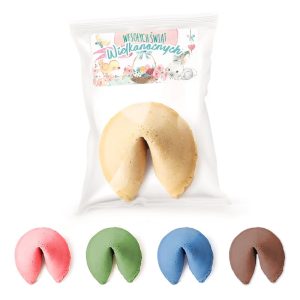 Tradycyjne ciasteczko wróżby w kolorze beżowym z opakowaniem świątecznym: "Wesołych Świąt Wielkanocnych", obok niego kolorowe ciasteczka w odcieniach różowym, zielonym, niebieskim i brązowym.