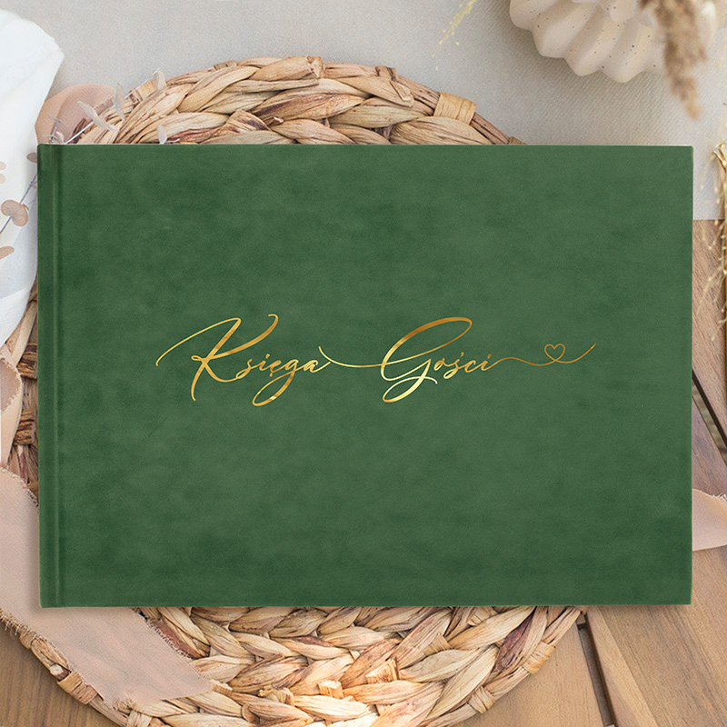 Zielona okładka książki z zachwycającym, złotym napisem 'Księga Gości' na tle plecionego kosza oraz jasnej tkaniny.