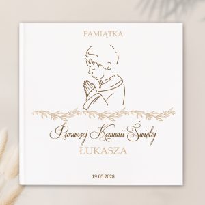 Okładka książki pamiątkowej z napisem 'Pamiątka Pierwszej Komunii Świętej Łukasza', przedstawiająca kontur chłopca modlącego się z rękami złożonymi, otoczona dekoracyjnym motywem roślinnym, z datą 19.05.2028.