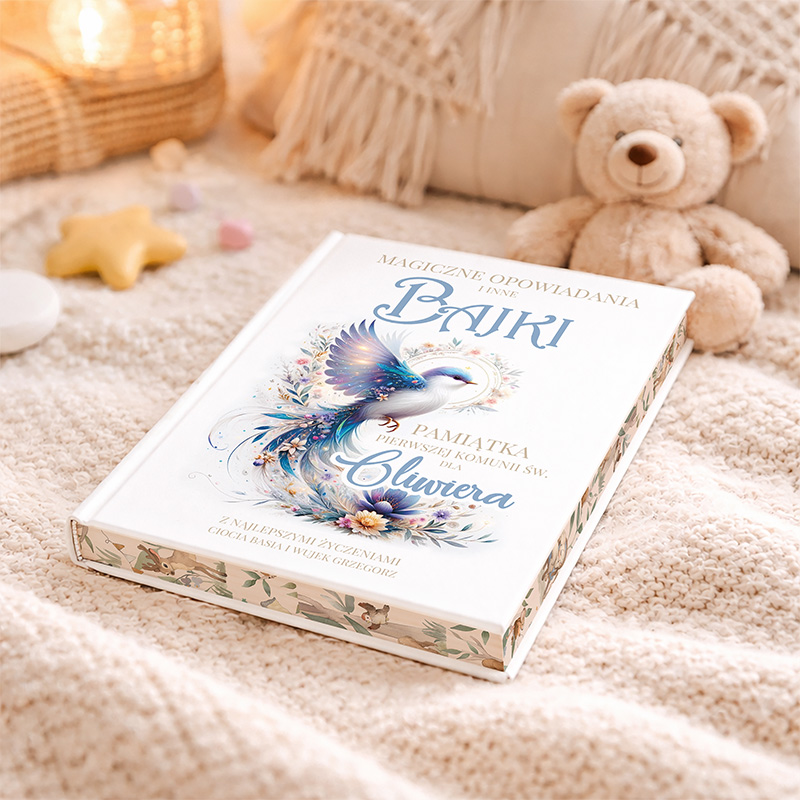 Książka o tytule 'Magiczne opowiadania i inne bajki' leży na miękkim kocyku, obok znajduje się pluszowy miś. Okładka książki zdobiona jest ilustracją kolorowego ptaka otoczonego kwiatami, a na niej napis 'Pamiątka Pierwszej Komunii św. dla Oliwiera'. W tle widać elementy dekoracyjne takie jak świeczki i zawieszki w kształcie gwiazdy.