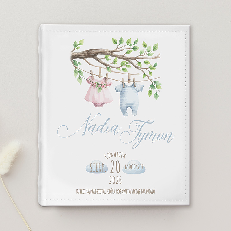 Okładka albumu dla dziecka przedstawiająca gałąź z kwiatami i wieszakiem z różowym i niebieskim ubrankiem, z napisem 'Nadia Tymon' oraz datą '20 sierpnia 2026', z cytatem o dzieciach jako nadziei.