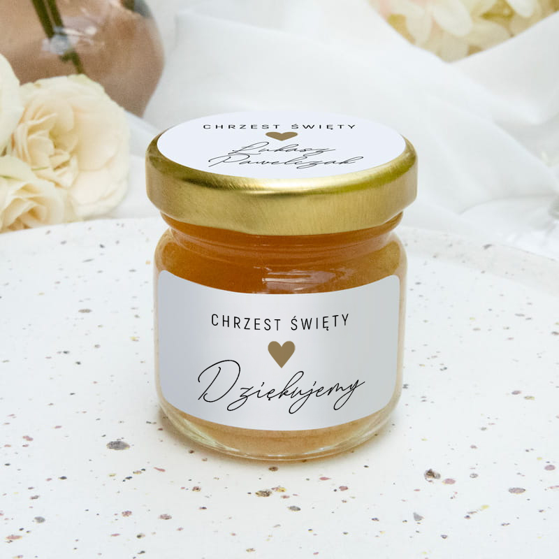 Słoik z miodem na jasnym tle, z etykietą z napisem 'Chrzcest Święty' i 'Dziękujemy', przykryty złotą zakrętką.