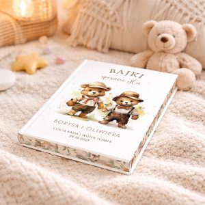 Książka zatytułowana "BAJKI spisane dla Borysa i Oliwiera" leży na miękkiej, białej kocyku wraz z pluszowym misiem w tle. Na okładce książki widoczne są dwa kreskówkowe misie w odzieży roboczej oraz ozdobny, roślinny wzór na dolnej krawędzi.