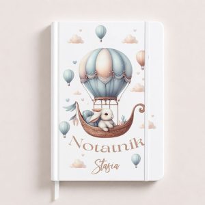 Notatnik z ilustracją przedstawiającą królika w balonie na gorące powietrze, otoczony chmurkami i balonami.