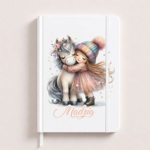 Notatnik z ilustracją dziewczynki w kolorowej sukience, przytulającej szarego jednorożca z kwiatową opaską. Na okładce napis "Madria".