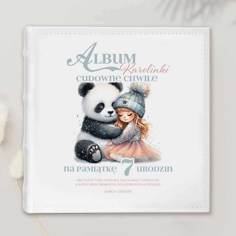 Okładka albumu ze zdjęciami, przedstawiająca dziewczynkę z długimi włosami w szarej sukience i czapce z pomponem, przytulającą dużego misia pandę. Na górze napis: 'Album Karolinki cudowne chwile' oraz 'na pamiątkę 7 urodzin'. Tło jest jasne, a całość ma delikatne, dziecięce akcenty.
