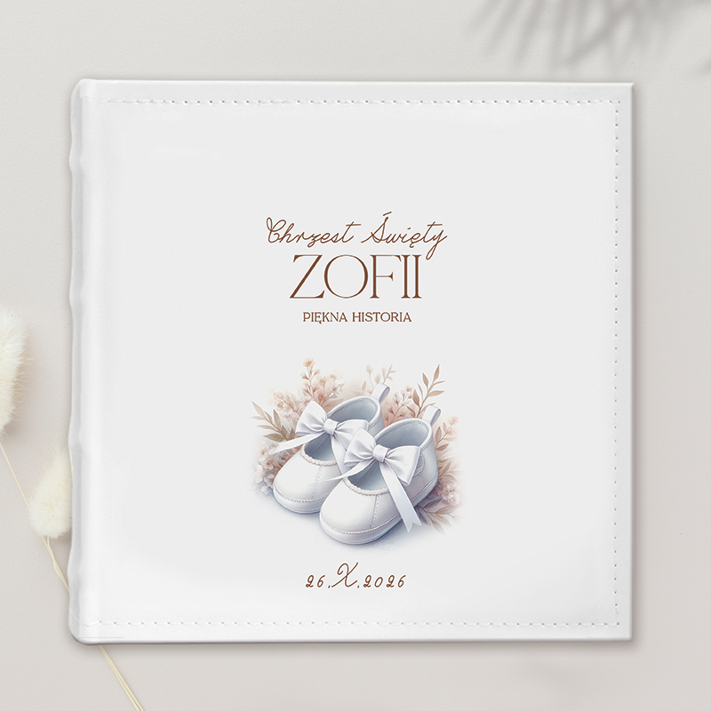 Biała okładka albumu na chrzciny z napisem "Chrzest Święty Zofii Piękna Historia" oraz ilustracją białych bucików z kokardkami, otoczonych delikatnymi kwiatami, z datą 26.X.2026.