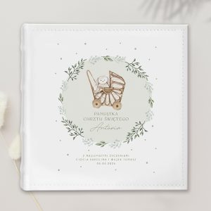 Biała okładka albumu na pamiątki z ilustracją dziecięcego wózka z pluszowym króliczkiem, otoczona zielonymi liśćmi. Na górze napis 'Pamiątka Chrztu Świętego Antosia', poniżej życzenia od 'Ciocia Karolina i Wujek Tomasz' oraz data 06.06.2026.