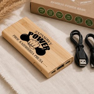 Bamboo power bank z napisem "ZAPASOWY POWER PRO. KAZIMIERZA PRUSKA" oraz dwoma portami USB i kablem do ładowania.