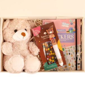zestaw-z-misiem-naklejki Zestaw prezentowy zawierający pluszowego misia w jasnym kolorze, opakowanie z kolorowymi cukierkami, pisak z rysunkiem misia oraz dwa notatniki - jeden o różowym tle ze świecącymi naklejkami, drugi czarny.