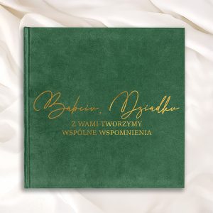 Zielona okładka albumu fotograficznego z napisem 'Babciu, Dziadku Z Wami Tworzymy Wspólne Wspomnienia' w złotym kolorze, leżąca na białym tle.
