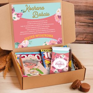 Otwarta teczka z prezentem dla babci, zawierająca kolorowy karton z napisem "Kochana Babciú" oraz różne czasopisma i pocztówki w środku, a obok leżą makaroniki na drewnianym tle.