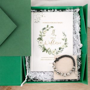 Zielone pudełko zawiera Biblię z roślinnym motywem oraz bransoletkę z kamieniami, wypełnione białym konfetti.