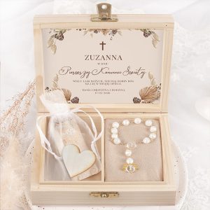 Drewniane pudełko z wyjątkowym zawartością na Pierwszą Komunię Świętą. Wewnątrz znajduje się dekoracyjny tekst zapraszający oraz bransoletka z perełkami. Obok bransoletki leży woreczek z sercem z drewna oraz inny mały przedmiot z grafiką. Tło ozdobione delikatnymi kwiatowymi motywami.