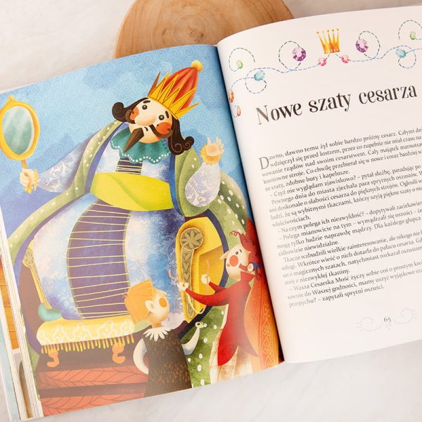 Ilustracja z książki przedstawiająca cesarza w kolorowej koronie, siedzącego na ozdobnym tronie i przeglądającego się w lusterku. W tle widać dwóch mężczyzn ubranych w różnokolorowe kostiumy, którzy z zainteresowaniem go obserwują. Tekst na stronie tytułowej to 'Nowe szaty cesarza'.