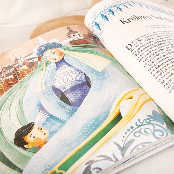 Ilustracja przedstawiająca Królową Śniegu z długimi, zielonymi włosami, ubrana w lodową suknię, trzymająca małego chłopca. W tle widać osadę z budynkami i drzewami.