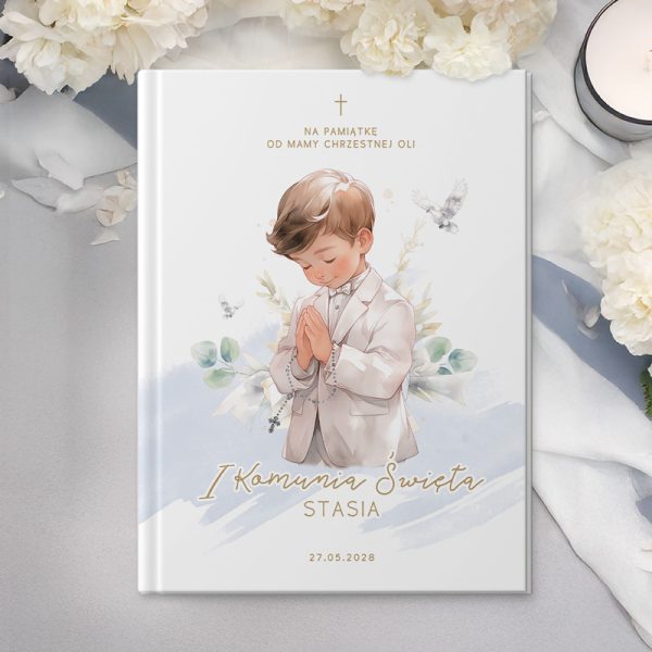 Okładka książki na pamiątkę z ilustracją chłopca w białym garniturze z złożonymi rękami, z tłem białych kwiatów i napisem "I Komunia Święta"