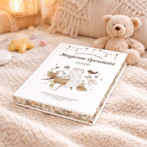 Książka zatytułowana "Magiczne Opowieści Hani" leży na miękkim, beżowym kocyku, obok pluszowego misia i dekoracyjnych gwiazdek. Okładka książki zdobiona jest ilustracjami, w tym koszykiem i różnymi elementami związanymi z dzieciństwem.