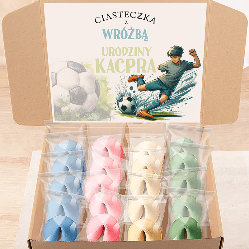 Elegancka pudełko z kolorowymi ciasteczkami wróżbami, wśród nich niebieskie, różowe, żółte i zielone, z ilustracją chłopca grającego w piłkę nożną i napisem "Ciasteczka z wróżbą Urodziny Kacpra" na pokrywie.