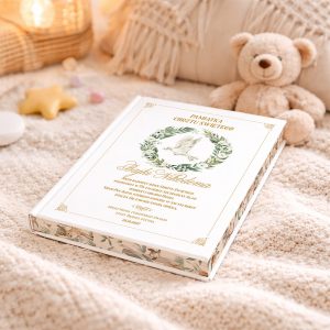 Księga pamiątkowa z białą oprawą, ozdobiona motywem zielonego wieńca z gołębiem i złotym napisem, leży na beżowym kocyku obok pluszowego misia i dekoracyjnych gwiazdek.