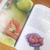 Ilustracja z kolorowych książek dla dzieci, przedstawiająca dwie wiewiórki na gałęzi drzewa oraz postać dziecka w kolorowej kurtce, stojącą wśród zielonych drzew i krzewów. W tle widać różowe jabłka na drzewie i miękką poduszkę z wiewiórkami śpiącymi na niej.