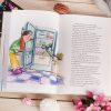 Strona książki z ilustracją przedstawiającą chłopca w zielonym swetrze i czerwonym szaliku, patrzącego do otwartej lodówki, z jej wnętrzem wypełnionym jedzeniem, w tym arbuzem. Obok znajduje się dłoń mrówki, a w tle widać różowe ciastka i kwiaty na tle drewnianego stołu.