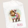 Ilustracja uroczej kapibary noszącej kolorowy sweter z sercami oraz czapkę z pomponem, z pięknym tłem w pastelowych kolorach, z napisem "MAJKA" na dole.