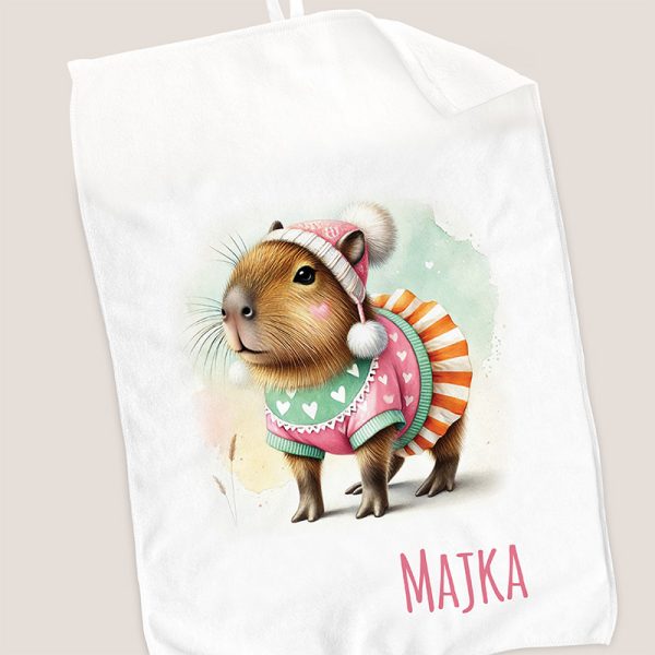 Ilustracja uroczej kapibary noszącej kolorowy sweter z sercami oraz czapkę z pomponem, z pięknym tłem w pastelowych kolorach, z napisem "MAJKA" na dole.