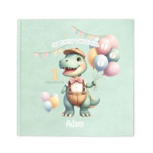 Ilustrowana okładka książki z zielonym dinozaurem w kapeluszu, trzymającym balony, z napisem "W DNIU TWOICH 1 URODZIN Adam" w kolorze pastelowym, z dekoracyjnymi flagami w tle.